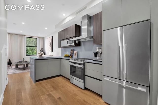 kitchen with appliances with stainless steel finishes, a sink, wall chimney exhaust hood, visible vents, and modern cabinets