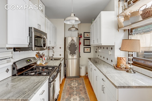 kitchen featuring white cabinets, appliances with stainless steel finishes, a sink, light wood finished floors, and tasteful backsplash