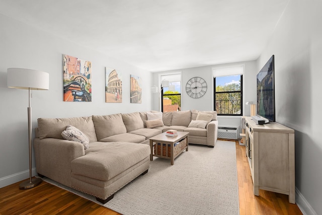 living area featuring light wood-style floors, baseboards, and a wall mounted AC