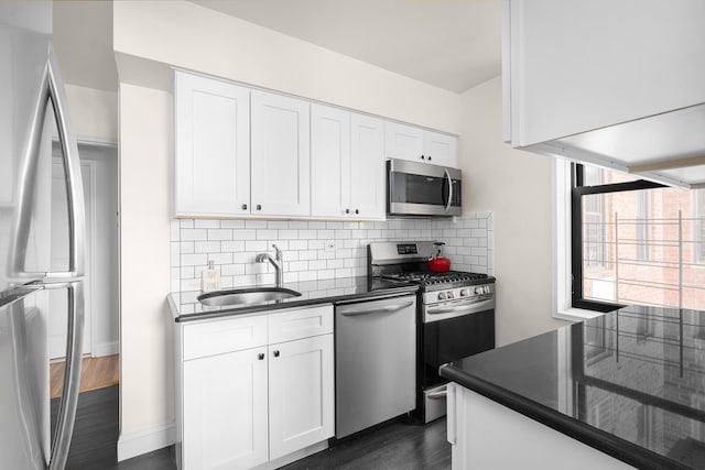 kitchen featuring white cabinets, stainless steel appliances, dark countertops, and a sink