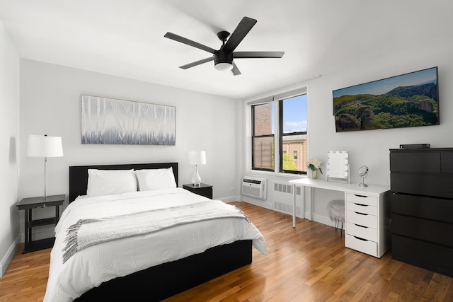 bedroom featuring baseboards, a wall mounted air conditioner, radiator heating unit, and light wood-type flooring