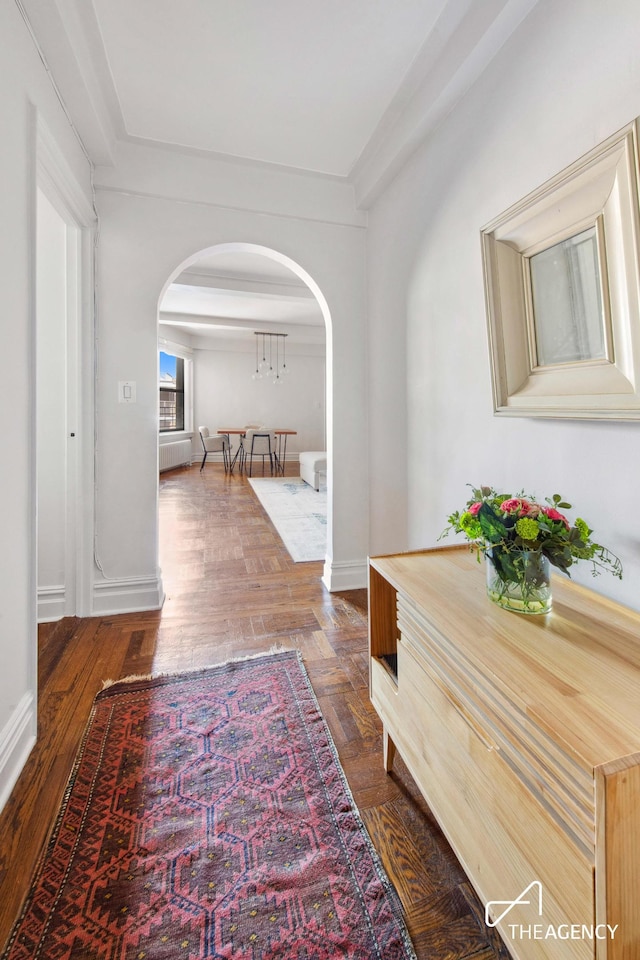 hall featuring arched walkways, baseboards, and dark wood finished floors