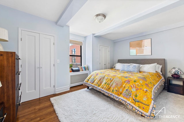bedroom featuring wood finished floors, baseboards, multiple closets, and beam ceiling