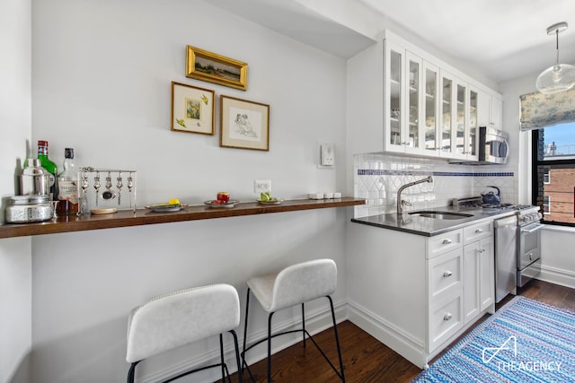 kitchen featuring glass insert cabinets, dark wood-style floors, tasteful backsplash, a sink, and appliances with stainless steel finishes