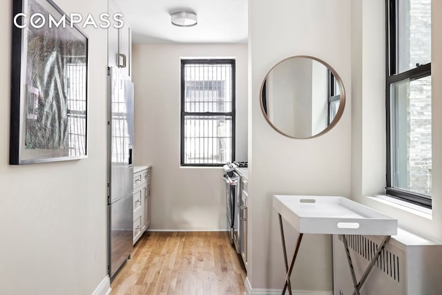 clothes washing area with baseboards, stacked washer and dryer, and light wood-style flooring