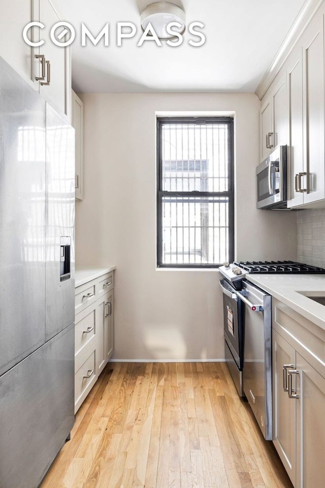 kitchen with light wood-style floors, light countertops, appliances with stainless steel finishes, and backsplash
