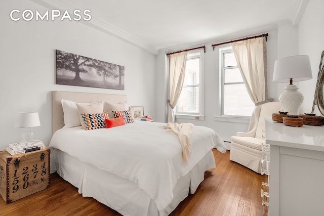 bedroom featuring ornamental molding, a baseboard heating unit, and wood finished floors