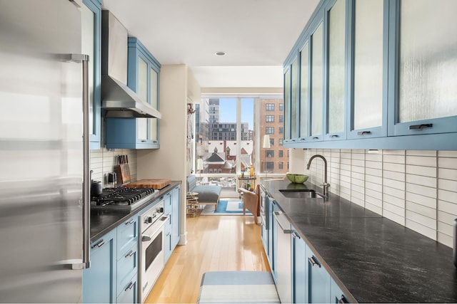 245 W 99th St Unit 7B, New York City, NY 10025 - kitchen with stainless steel appliances, blue cabinets, wall chimney exhaust hood, a sink, and backsplash