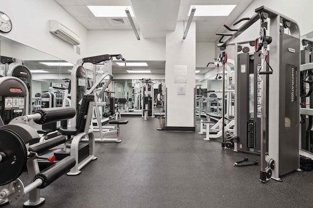exercise room with visible vents, a wall mounted air conditioner, a paneled ceiling, and a towering ceiling