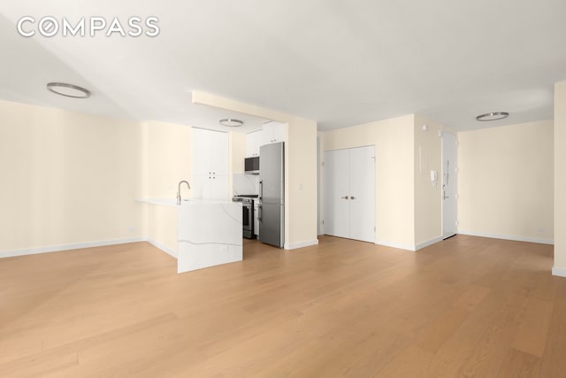 unfurnished living room featuring baseboards, a sink, and light wood finished floors