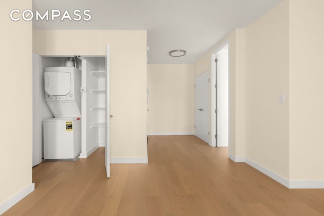 laundry room with laundry area, light wood finished floors, stacked washing maching and dryer, and baseboards