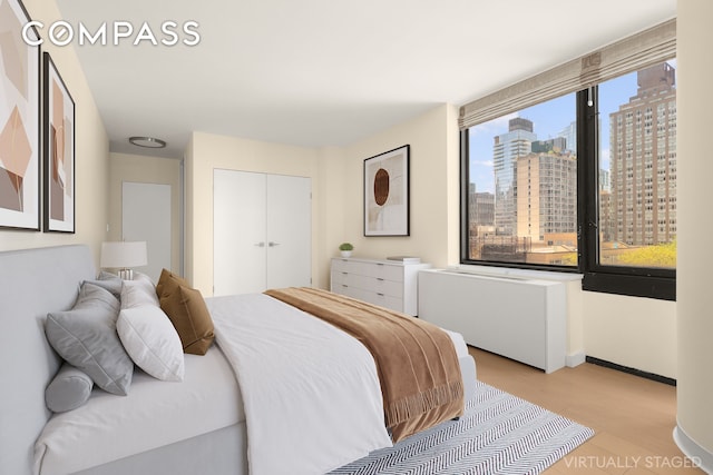 bedroom with a view of city, baseboards, a closet, radiator, and light wood-style flooring