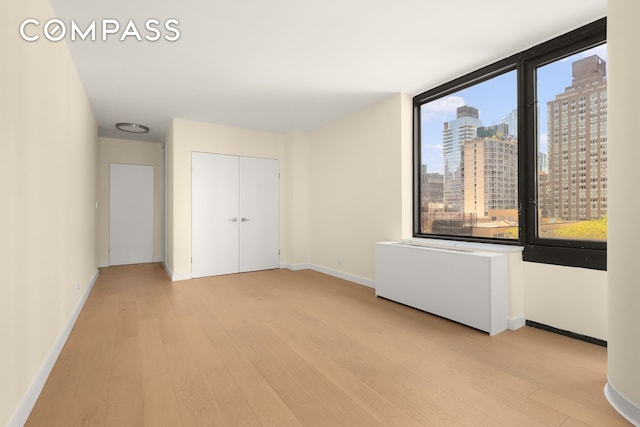 empty room featuring a view of city, baseboards, and light wood-type flooring