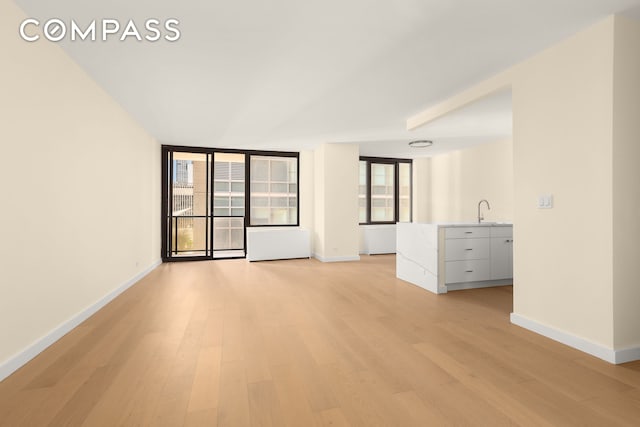 unfurnished living room with baseboards, a sink, and light wood finished floors