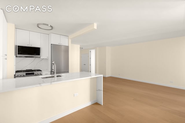 kitchen with baseboards, light wood-type flooring, white cabinetry, a sink, and stainless steel appliances