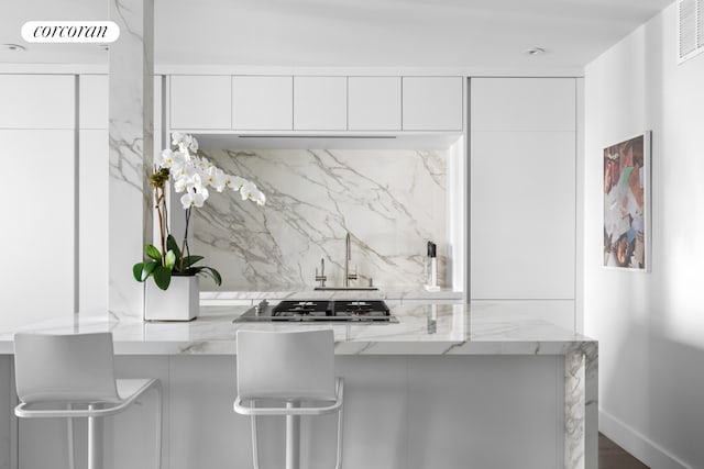 kitchen featuring decorative backsplash, modern cabinets, stainless steel gas cooktop, light stone counters, and white cabinetry