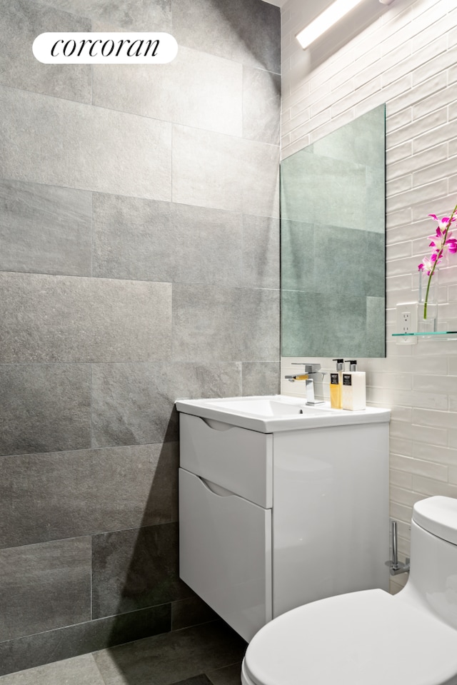 bathroom featuring toilet, tile walls, and vanity