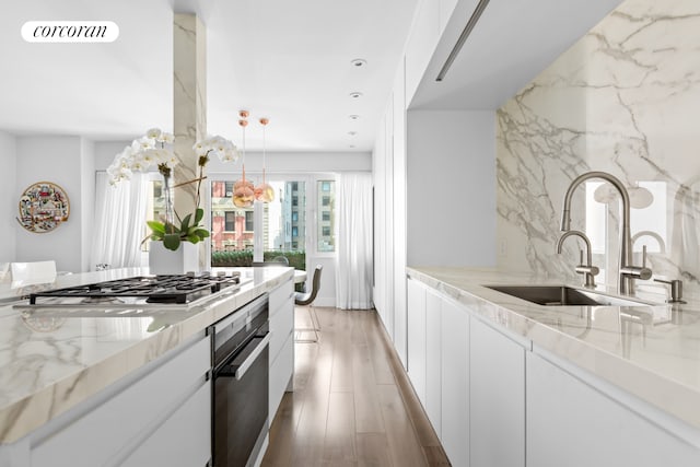 kitchen with light stone counters, appliances with stainless steel finishes, a sink, light wood-style floors, and visible vents
