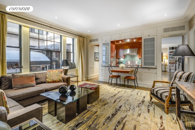 living area with visible vents, ornamental molding, and light wood-style flooring