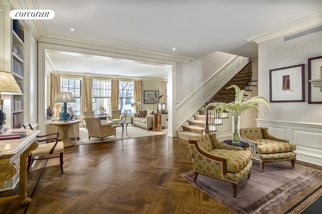 sitting room with crown molding, visible vents, stairs, and a decorative wall