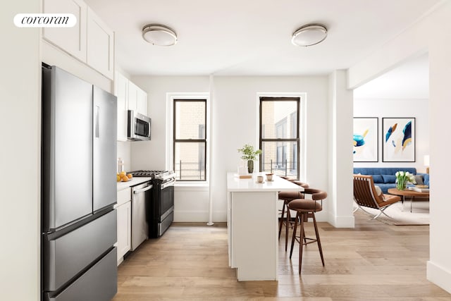 3000 Valentine Ave Unit 5J, New York City, NY 10458 - kitchen featuring appliances with stainless steel finishes, a kitchen breakfast bar, light wood finished floors, white cabinetry, and light countertops