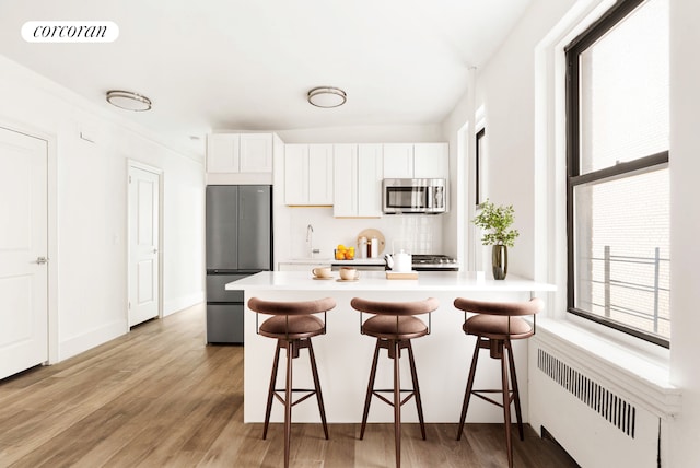 3000 Valentine Ave Unit 5J, New York City, NY 10458 - kitchen featuring appliances with stainless steel finishes, radiator heating unit, a breakfast bar area, and light wood-style floors