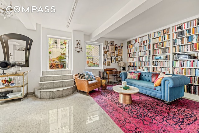sitting room featuring granite tiled floors, beamed ceiling, bookshelves, and baseboards