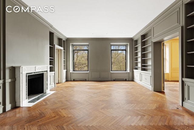 unfurnished living room with built in shelves, crown molding, a fireplace, and a decorative wall
