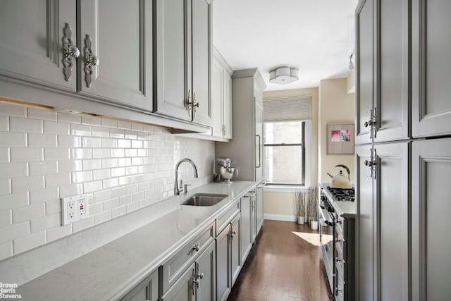 kitchen with a sink, high end stainless steel range oven, gray cabinetry, decorative backsplash, and baseboards
