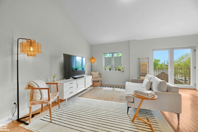 living area featuring high vaulted ceiling, light wood finished floors, and baseboards