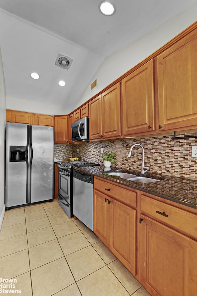 kitchen with appliances with stainless steel finishes, a sink, lofted ceiling, tasteful backsplash, and light tile patterned floors