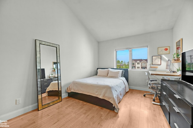 bedroom featuring an office area, light wood-style floors, baseboards, and high vaulted ceiling