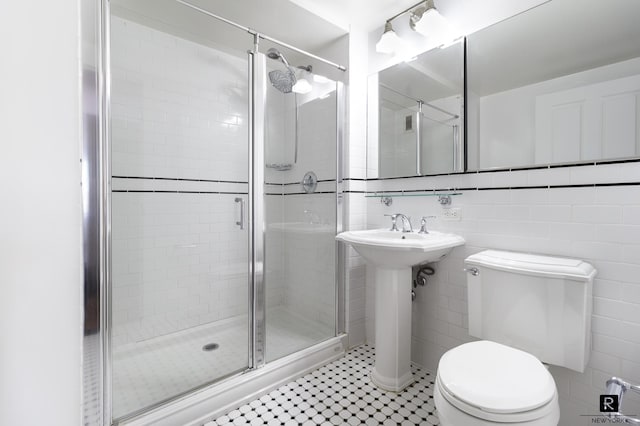 bathroom with a stall shower, toilet, a sink, and tile walls