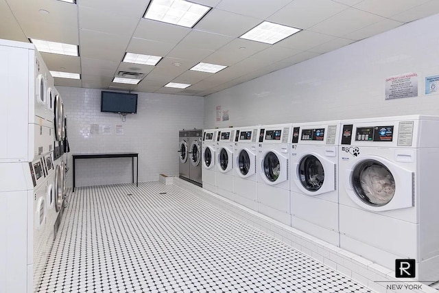 shared laundry room with stacked washing machine and dryer, washer and dryer, and tile walls