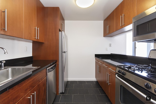 kitchen featuring appliances with stainless steel finishes, dark tile patterned flooring, a sink, dark countertops, and baseboards