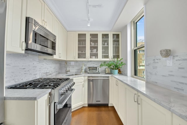 575 Main St Unit 1611, New York City, NY 10044 - kitchen with stainless steel appliances, a sink, rail lighting, tasteful backsplash, and glass insert cabinets