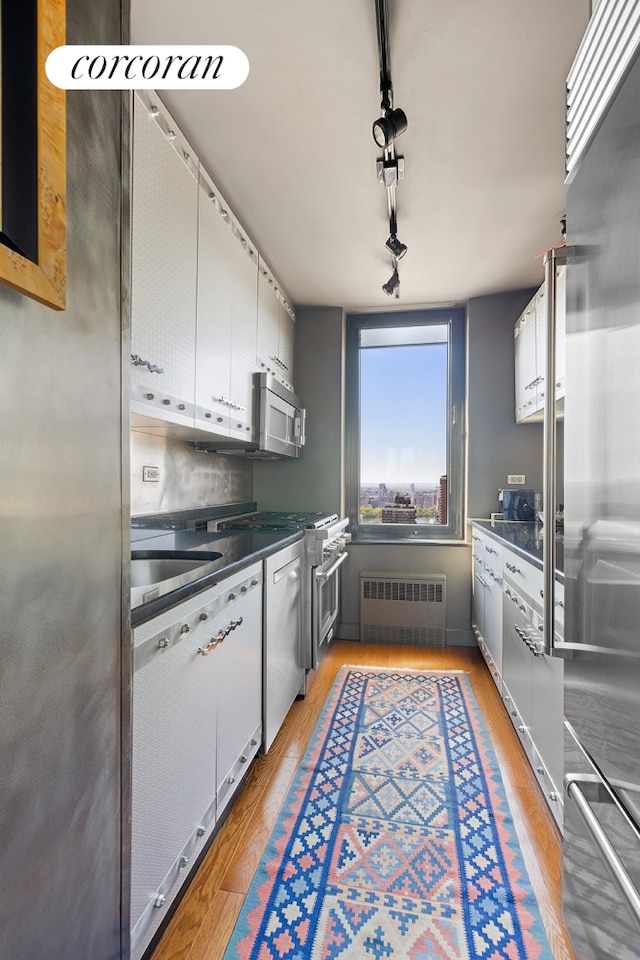 kitchen featuring high end appliances, radiator heating unit, light wood-style floors, and rail lighting