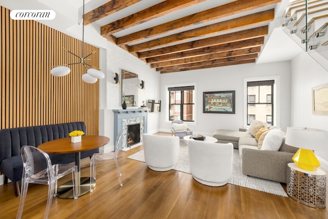 living room with wood finished floors, beamed ceiling, a tiled fireplace, and stairs