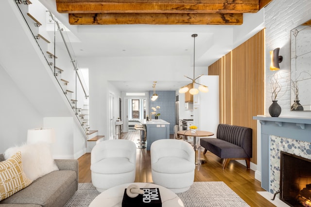 living room featuring wood finished floors, stairs, a tiled fireplace, baseboards, and beamed ceiling