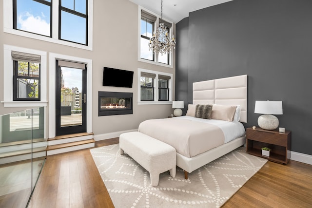 bedroom with baseboards, access to outside, wood finished floors, a chandelier, and a towering ceiling
