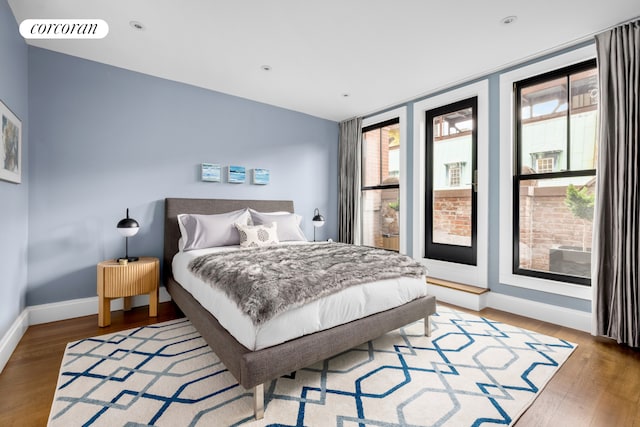 bedroom with multiple windows, wood finished floors, and baseboards