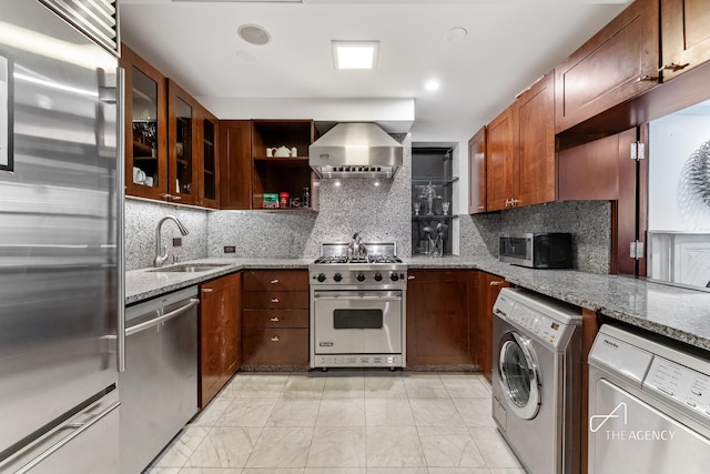 kitchen featuring high end appliances, washer / dryer, wall chimney range hood, and light marble finish flooring