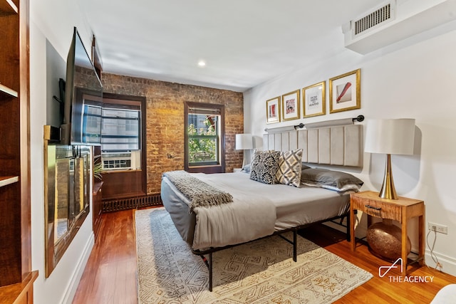 bedroom featuring wood finished floors, brick wall, and recessed lighting