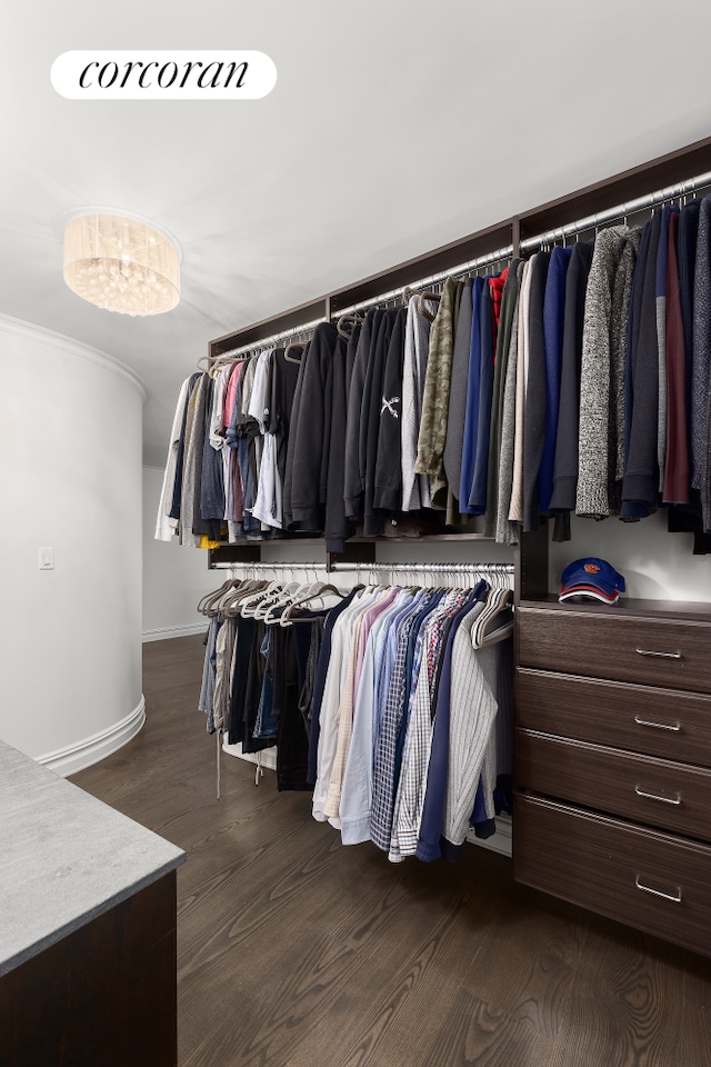 spacious closet with dark wood-style floors and a chandelier