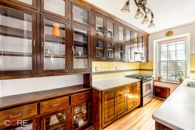 kitchen with glass insert cabinets, light wood-style flooring, backsplash, stainless steel gas range oven, and white microwave