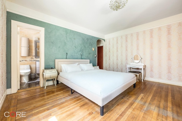 bedroom with wallpapered walls, ensuite bath, baseboards, and hardwood / wood-style floors