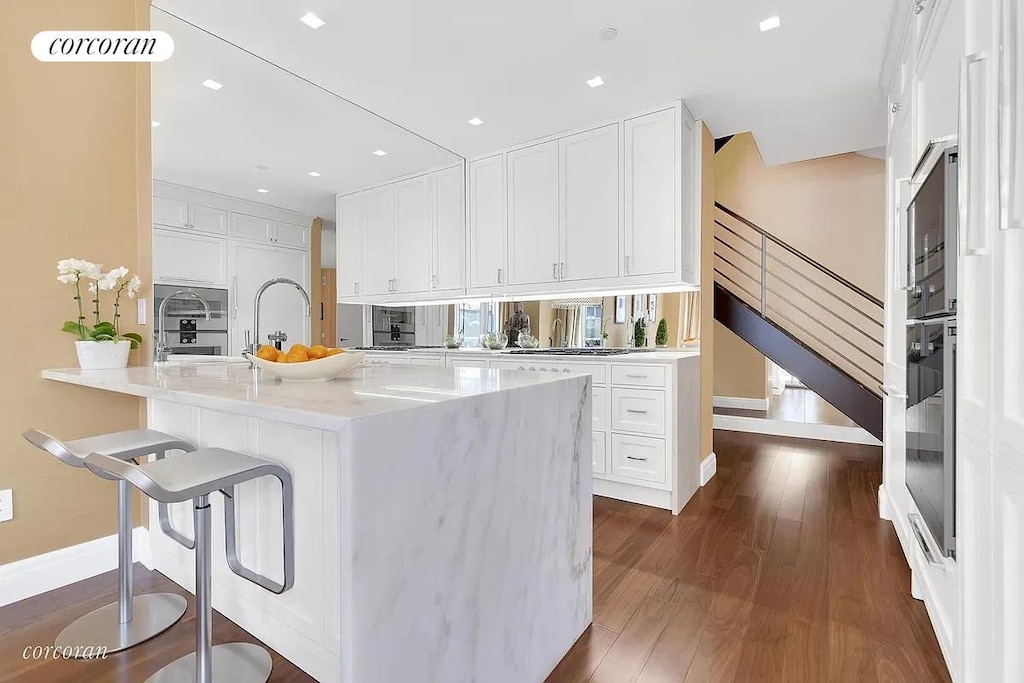 kitchen with baseboards, dark wood-style floors, white cabinetry, light countertops, and a kitchen breakfast bar