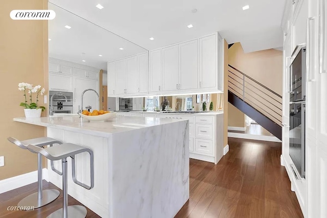 kitchen with baseboards, dark wood-style floors, white cabinetry, light countertops, and a kitchen breakfast bar