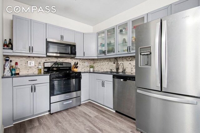 kitchen featuring stainless steel appliances, a sink, dark countertops, light wood finished floors, and decorative backsplash