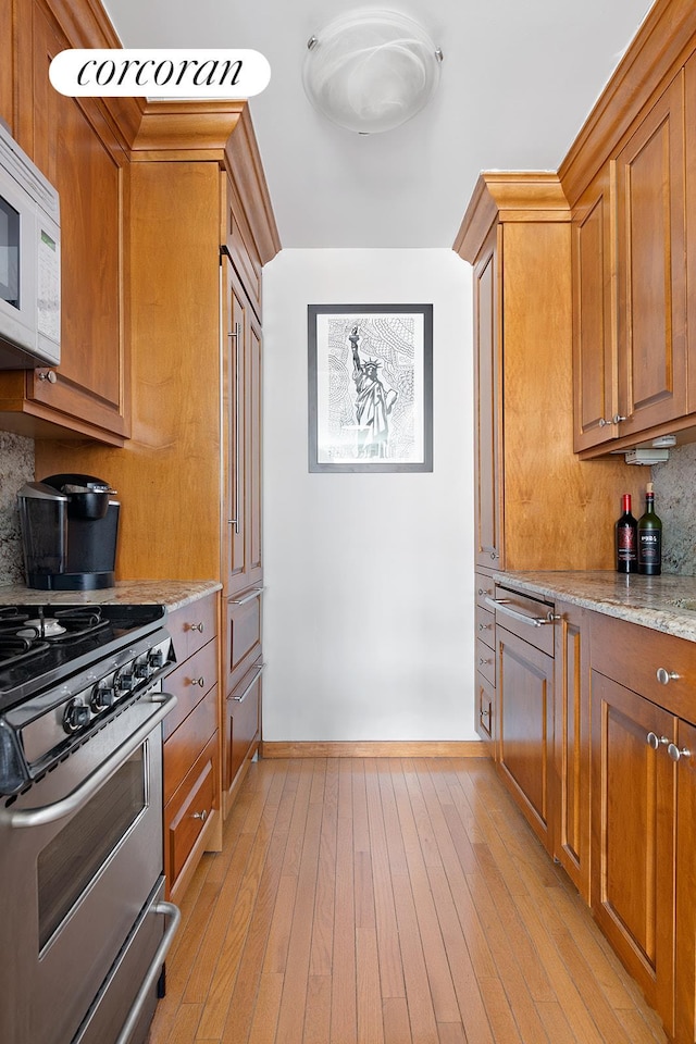 kitchen featuring gas range, white microwave, brown cabinets, backsplash, and light wood-type flooring